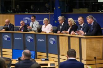 A group of senior political officials sits at a long table during a press conference in Brussels