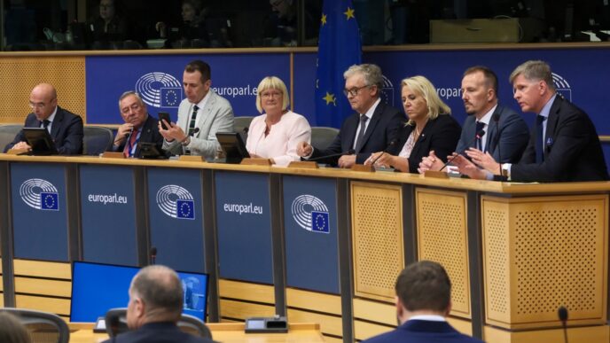 A group of senior political officials sits at a long table during a press conference in Brussels