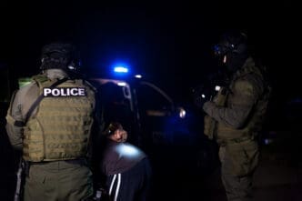 Police officers detain a person at night, with police car lights flashing