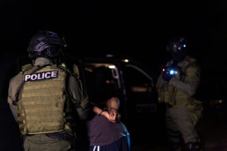 Two police officers in tactical gear arrest a person on a dark night