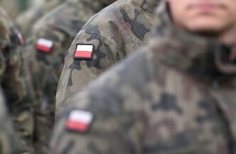 A close-up of a Polish flag patch on the sleeve of a soldier's camouflage uniform