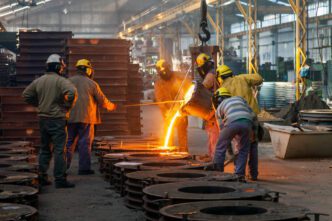 Foundry workers in safety gear pouring a stream of molten metal into a row of molds