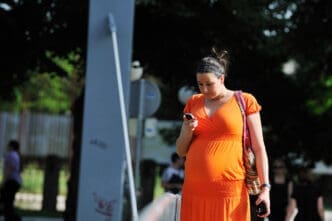 Pregnant woman in an orange dress walking outdoors and using her phone