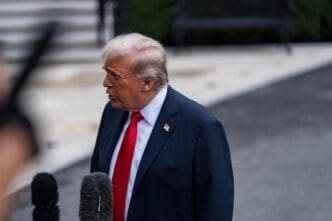 President Donald J. Trump speaks to the press outdoors, framed by microphones in the foreground