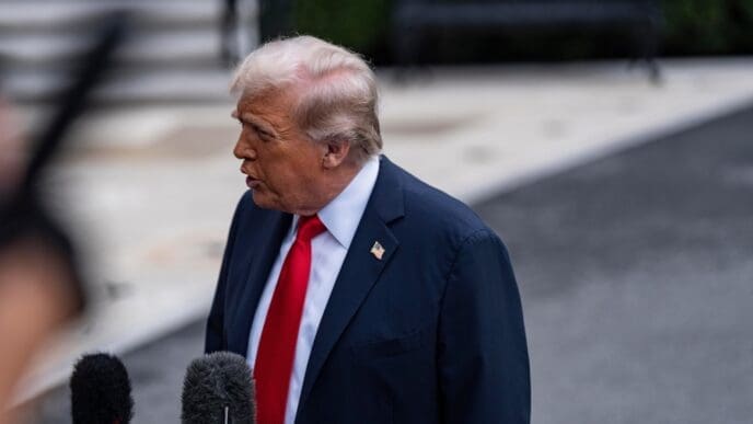 President Donald J. Trump speaks to the press outdoors, framed by microphones in the foreground