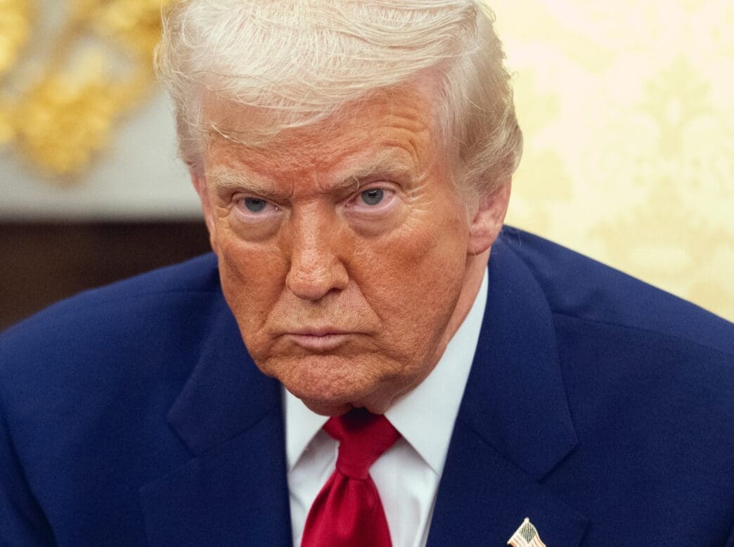 Donald Trump seated at a table, looking ahead with a serious, focused expression