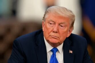 United States President Donald Trump is shown in a close-up, head-and-shoulders portrait, looking away from the camera with a serious expression