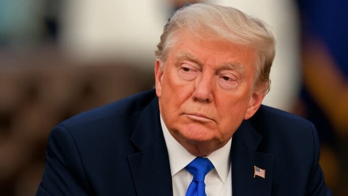 United States President Donald Trump is shown in a close-up, head-and-shoulders portrait, looking away from the camera with a serious expression