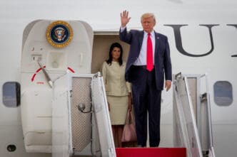 President Donald Trump waves as he disembarks Air Force One with a woman beside him