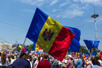 Crowd waving Moldovan and EU flags under a blue sky