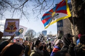 Protesters hold Tibetan flag and signs outside a modern building under a bright sky