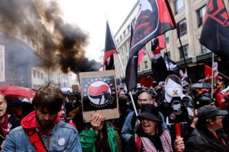 People protesting against the far right, holding signs and flags with smoke in the background