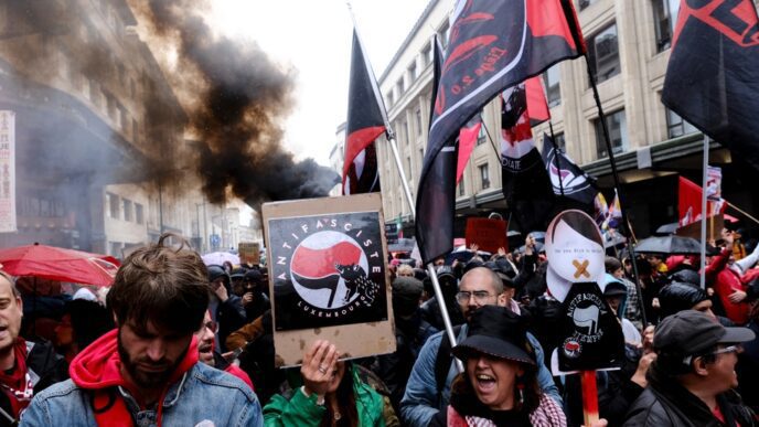 People protesting against the far right, holding signs and flags with smoke in the background