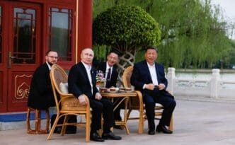 Vladimir Putin and Xi Jinping are seated with two other men at a small table outside