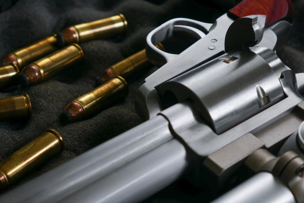 Close-up of a silver revolver and scattered brass bullets on a dark surface