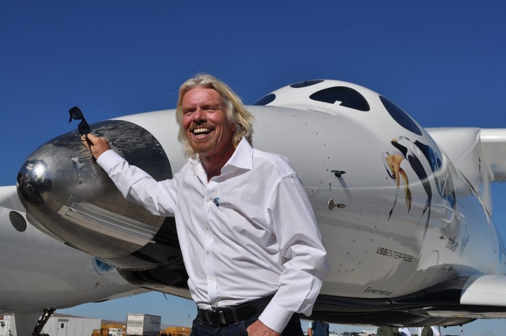 Richard Branson smiles broadly while standing in front of a Virgin Galactic spaceship