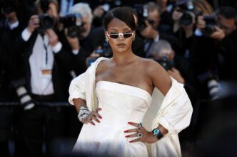 Rihanna wears a white strapless dress and matching jacket on the red carpet, striking a pose