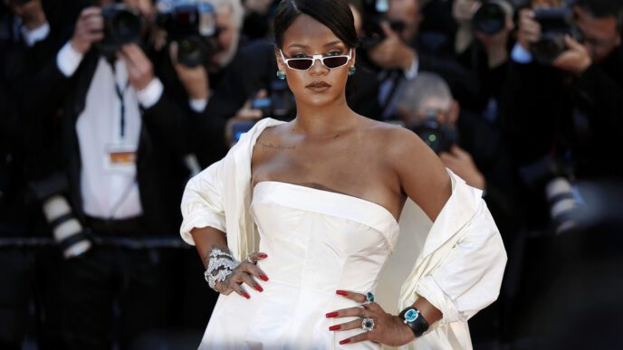 Rihanna wears a white strapless dress and matching jacket on the red carpet, striking a pose