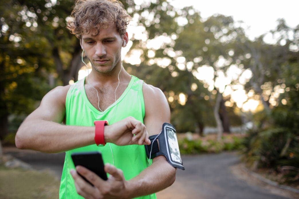 Man in green tank top checks smartwatch while holding phone
