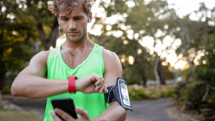 Man in green tank top checks smartwatch while holding phone