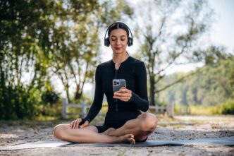 A woman in athletic wear is meditating outdoors with headphones and a smartphone