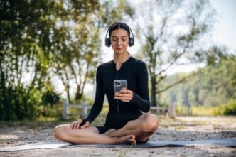 A woman in athletic wear is meditating outdoors with headphones and a smartphone