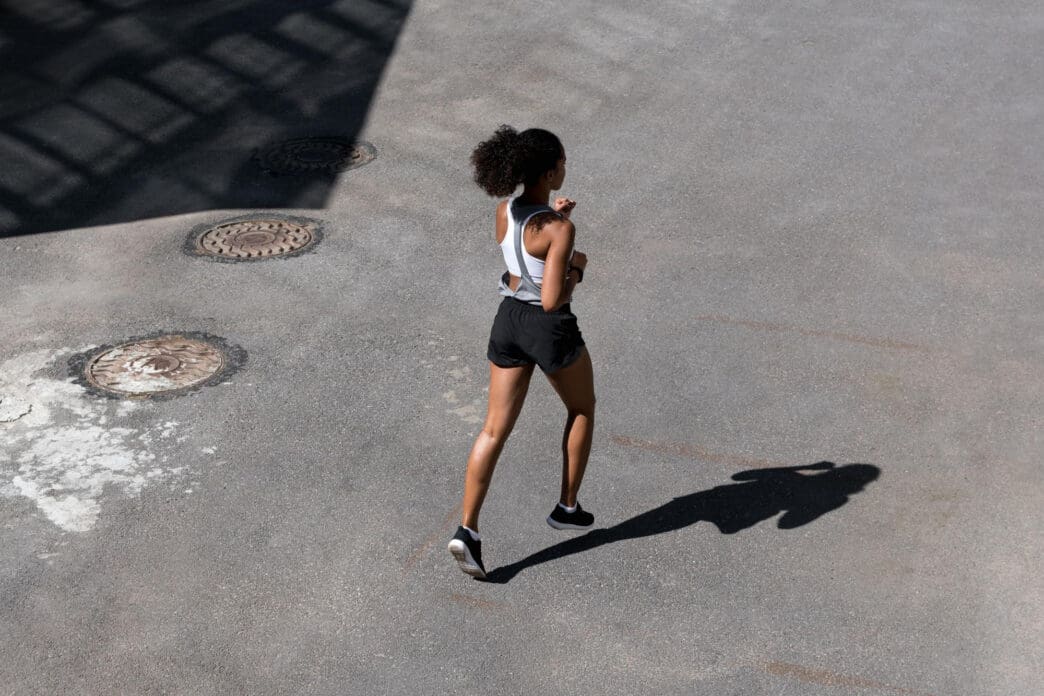 Woman with curly hair runs on pavement with manhole covers