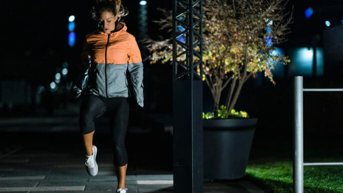 A woman in a running jacket and leggings performs a nighttime exercise on a paved path in Miami