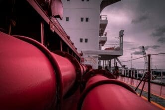 Red pipes and white superstructure of an LNG ship under a cloudy sky
