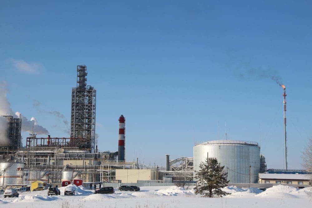 An oil refinery in a snowy landscape with smoke stacks and a burning flare