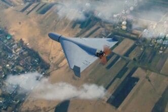 A 3D render shows a gray military kamikaze drone flying over a rural landscape with clouds and smoke