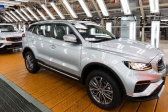 Silver Chery SUV on a yellow platform in a factory with bright lights