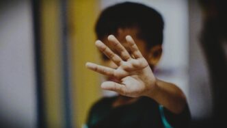 A child's hand raised in a "stop" gesture, with their face blurred in the background