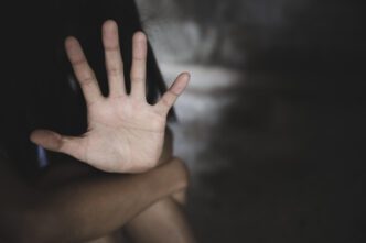 A person making a 'stop' gesture with their hand, against a dark, blurred background