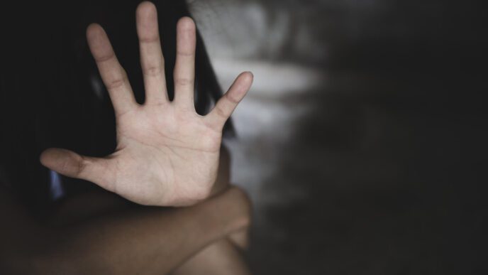 A person making a 'stop' gesture with their hand, against a dark, blurred background