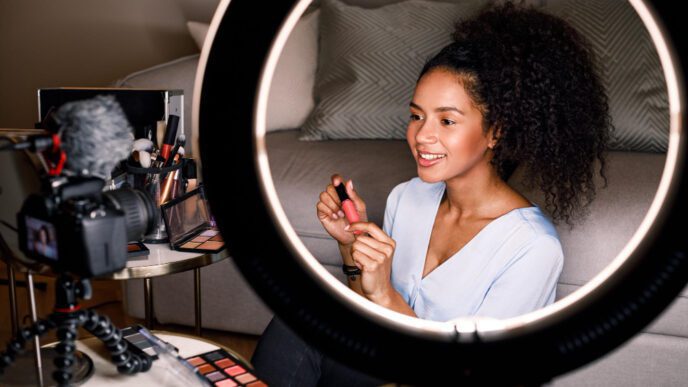 A female influencer holding a lip gloss and speaking to a camera, framed by a ring light