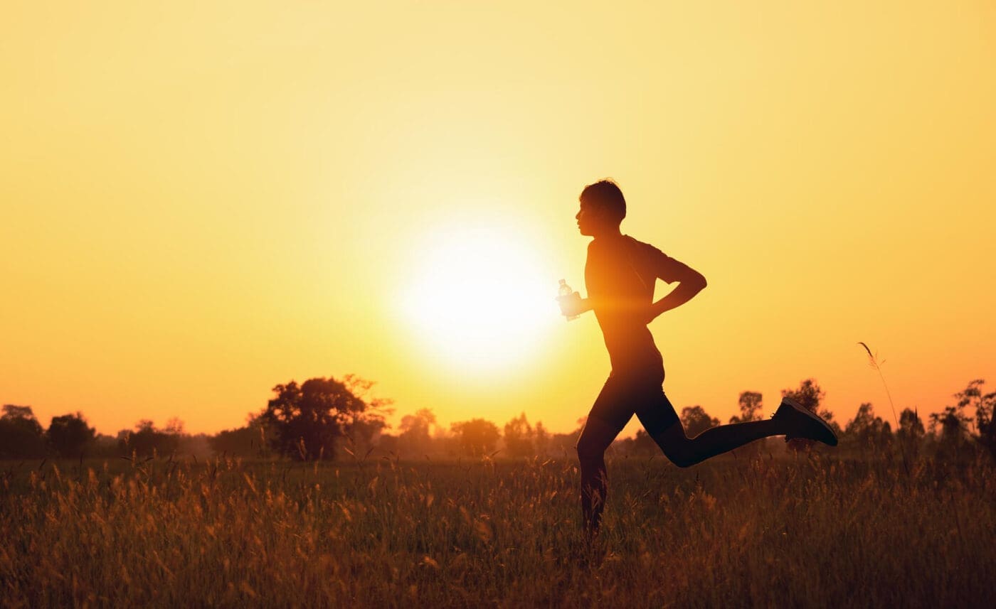 Silhouette of a person running with a water bottle at sunset