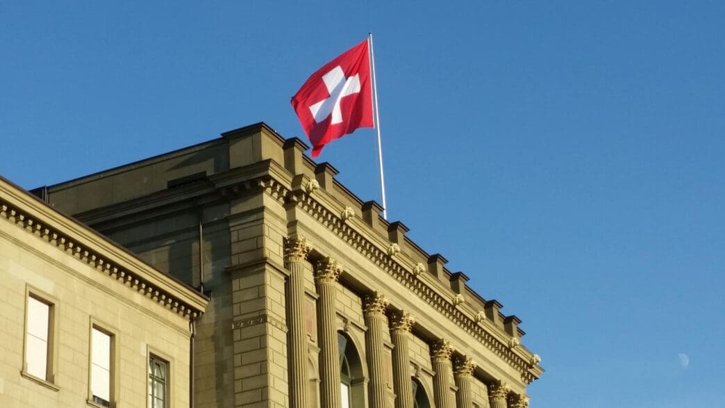 Swiss flag flying on a pole atop a classical building in Switzerland
