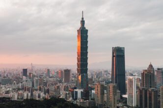 The Taipei 101 skyscraper is illuminated by the sunset in a dense, hazy urban landscape