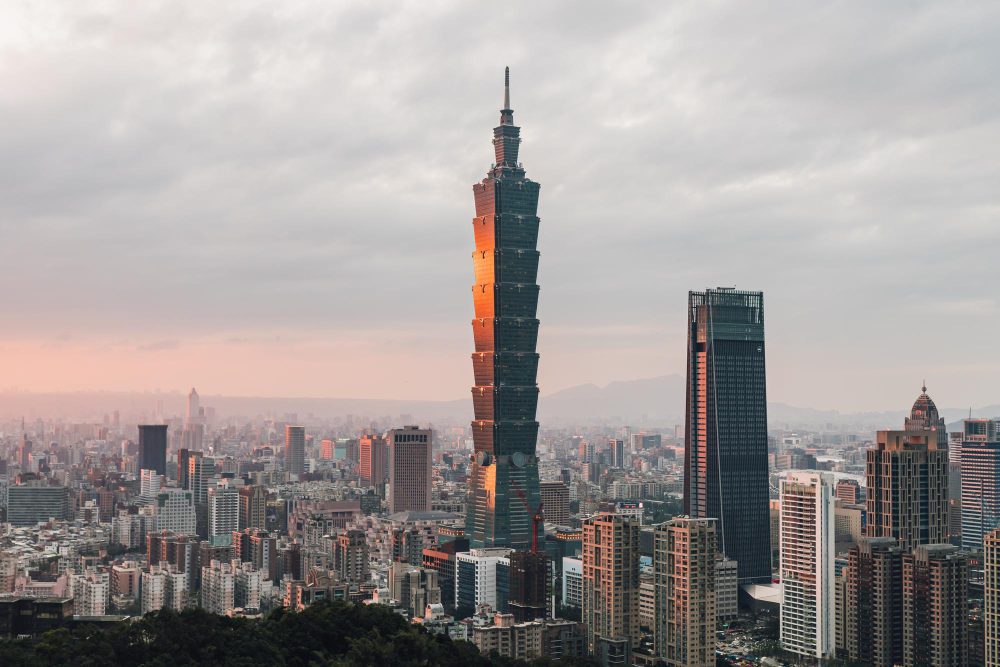 The Taipei 101 skyscraper is illuminated by the sunset in a dense, hazy urban landscape