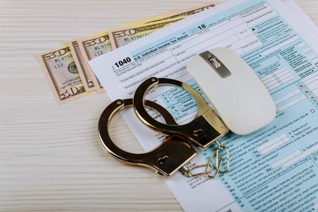 Handcuffs, computer mouse, and money on a tax form
