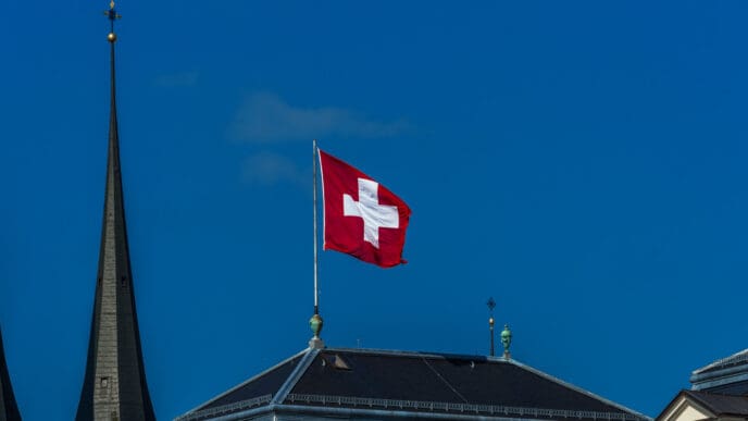 The square red flag of Switzerland with its prominent white cross waves on a flagpole atop a dark roof