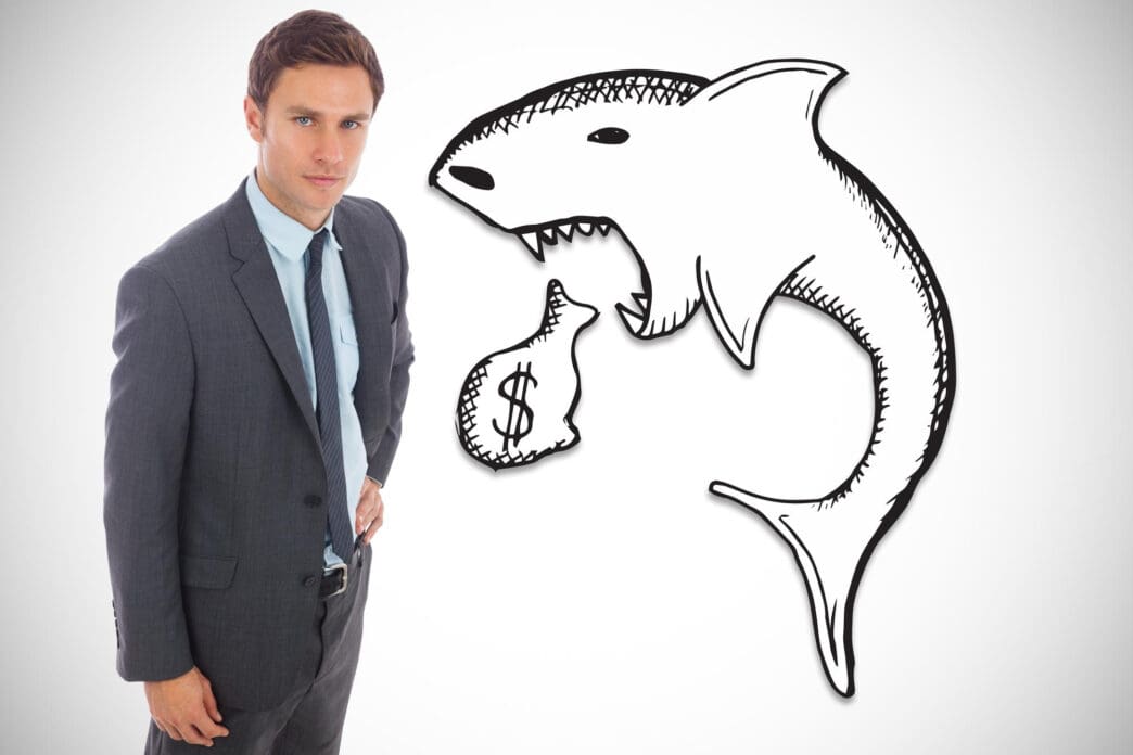 Businessman standing next to a drawing of a shark about to eat a money bag
