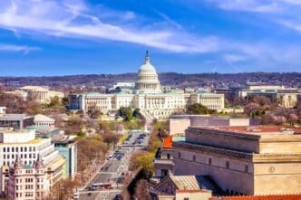 A high-angle, panoramic view of the United States Capitol Building and its surrounding cityscape under a blue sky
