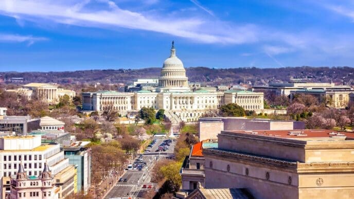 A high-angle, panoramic view of the United States Capitol Building and its surrounding cityscape under a blue sky