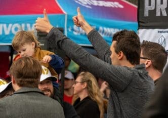 People give thumbs up and a child sits on a person's shoulders at a political event