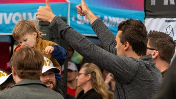 People give thumbs up and a child sits on a person's shoulders at a political event