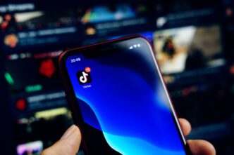 A person holds a smartphone with the TikTok app icon visible on the screen