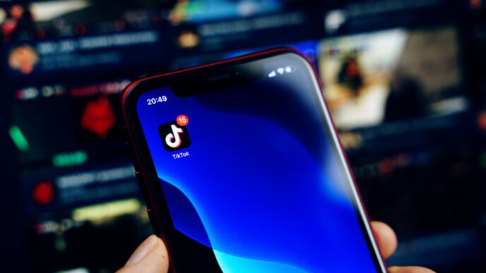 A person holds a smartphone with the TikTok app icon visible on the screen
