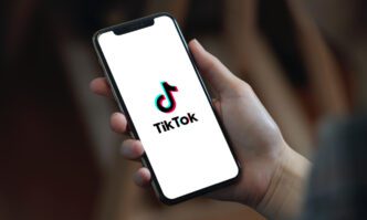 A person is holding a smartphone displaying the TikTok logo on its screen